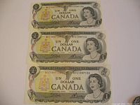 Three Canadian one dollar bills laid out stacked: 1973 series, serial numbers BFE1997130, BFE1997131, BFE1997132, showing front side with portrait of Queen Elizabeth II and coat of arms.