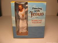 Front of packaging showing 3-inch dancing Jesus bobbling figurine in white robe inside box.