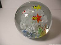 Clear spherical glass paperweight showing colorful glass fish and numerous bubbles encapsulated inside, with underwater flora details at the base.