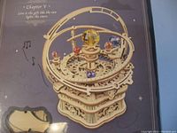 Close-up photo of the assembled mechanical music box model showing intricate wooden gears, rotating mechanisms, central globe, and star-themed decorations.