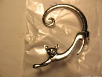 Silver cat-shaped ear wrap earring viewed from front and side, showing detailed cat face, outstretched front paws, and curled tail design