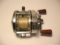 Side view of Shimano Bantam 100 bait casting reel showing wooden handles and chrome finish, line on spool visible