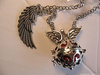 Close-up of the silver-tone pendant with wings and feather design showing the red harmony ball inside the locket cage pendant.