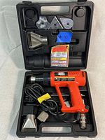 Black & Decker Heat Pro Deluxe heat gun in black molded plastic case with multiple metal heat nozzles and a small instruction manual.