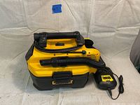 Top front angled view of yellow and black DEWALT DCV581H vacuum with hose and charger on side.