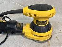 Front angle view of DEWALT sander showing yellow and black housing, power cord, and dust bag.