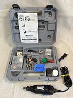 Dremel 200 rotary tool kit open in grey plastic case with accessories and instruction manual.