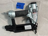 Side view of Hitachi NT50AE2 brad nailer showing the air inlet, handle grip, and safety warnings.