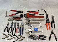 Full lot of pliers, wrenches, cutters displayed on light cloth backdrop, showing variety of tool types and brands.