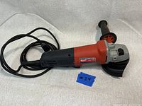 Side view of Milwaukee 6148-30 4 1/2 inch angle grinder showing red and black body, side handle, and power cord coiled behind.