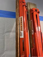 Close-up of the orange metal frame of the Tote-A-Horse sawhorse and brand label attached to wooden plank