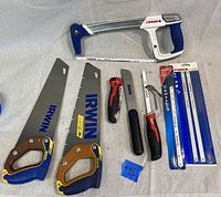 Full view of all saw and cutting hand tools laid out on fabric, includes Irwin saws, Lenox hacksaw, Milwaukee hacksaw, utility knife, and packaged saw blades