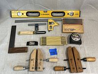 Image showing entire lot of woodworking tools arranged on a surface including level, clamps, sharpening stone, tape measure and squares.