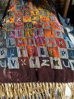 Full view of scarf showing multi-colored velvet alphabet squares on black silk chiffon background with hand knotted silk fringe at the end.
