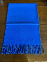 Blue scarf folded on wooden surface showing body and fringed end