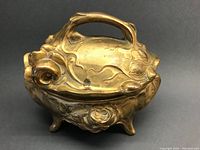 Full view of the brass Art Nouveau trinket box showing the organic shapes, hinged lid with branch handle, and four rounded legs.