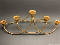 Overall view of gold plated candelabra with five candle cups on arched rods laid flat