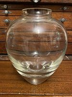 Front view of clear glass vessel, showing round body and thick solid glass base.