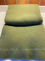 Folded olive green wool blanket showing texture and removed satin border with stitching.