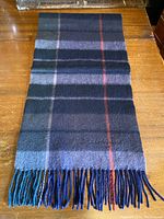 Full view of the rectangular navy blue plaid scarf laid flat on wooden surface, showing overall pattern and fringe.