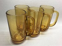 Four amber-colored glass beer mugs arranged in a group, showing the side and handles.
