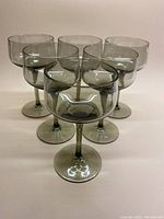 Photo shows six smoky grey stemmed aperitif glasses arranged in two rows on a plain surface.