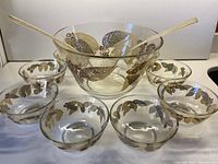 Full view of large salad bowl, 8 smaller bowls and gold flecked clear serving utensils showing leafy foliage and berry decoration.