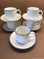 Set of 5 cream-colored cups and saucers with cinnamon speckles and rimmed edges, stacked and arranged to show all pieces.