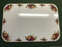 Top surface of a hot plate showing rounded corners and clusters of red and orange roses around edge on cream background.