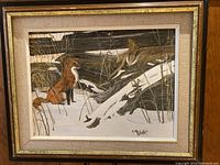 Framed oil painting showing a red fox standing among snowy fallen trees in a forest. The frame is wooden with a fabric matte inner border. Artist's signature visible lower right.