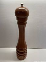 Full view of the wooden pepper grinder showing its tall, curved profile and wood grain.