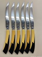 Full view of six serrated cutting knives laid out side-by-side showing blades and handles.