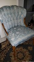 Front and side view of blue floral upholstery accent chair with tufted back and curved wooden arms and legs, showing detailed fabric pattern and wood finish.