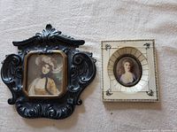 Front view of two antique miniature paintings featuring women, one in a black detailed carved frame and one in a cracked ivory-toned decorative frame.