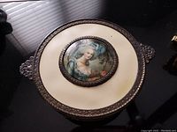 Top view of the candy dish lid showing the portrait medallion and bronze decorative rim with ivory Bakelite body.