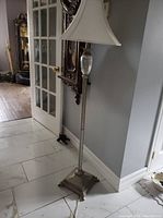Full view of floor lamp with fabric shade and crystal decoration against a wall and floor tiles