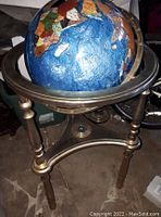 Full view of the globe on bronze metal stand showing the ocean and continents with the crack not easily visible.