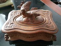 Top view of ornate wooden box showing carved bird figure on lid and floral decorations on edges
