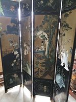 Four-panel folding room divider with black frame and gold accents, each panel illustrating traditional Asian scenes with figures and nature elements.