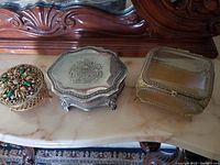 Three vintage jewelry boxes displayed closed on a marble surface showing their exterior designs.