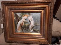 Photo of the oil painting on board showing two parrots perched on a branch, set within an ornate wooden gilt frame.