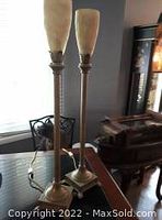 Pair of tall slag lamps with mottled beige slag glass shades atop metal stands, shown on a table near window.