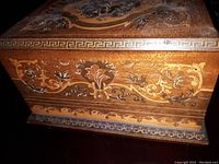 Close-up of ornate inlaid wood detailing on the side of the music box, showing floral and scroll designs with some wear consistent with age.