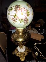 Full view of the vintage lamp with hand-painted floral globe and ornate brass base with marble accent.