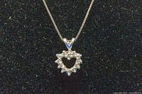 Front view of 14K white gold heart pendant with melee diamonds on black background to highlight sparkling details.