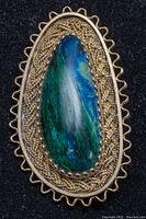 Close-up front view of the brooch/pendant showing the green Eilat cabochon stone with intricate silver filigree surrounding it.