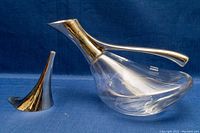 Front angle of duck-shaped crystal decanter with silver plated neck and separate silver plated pouring spout on a blue background