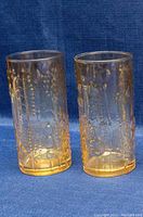 Two amber Iittala Flora tumblers showing embossed floral & geometric designs, amber tint