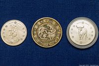 Photo showing three silver coins - rat coin on left, Japanese yen coin in middle with dragon design, ox coin on right in plastic case.