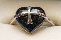 Close-up showing heart-shaped black stone with silver cross and twisted rope detail on the silver ring.